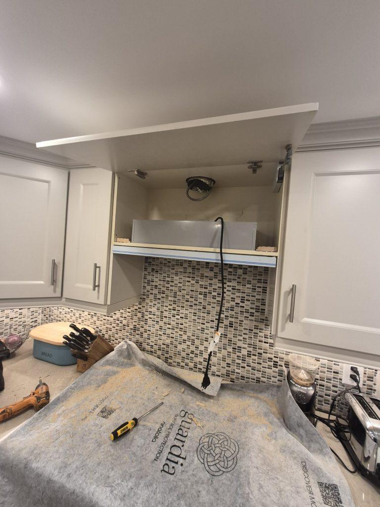 Built-in range hood insert being fitted inside a custom kitchen cabinet with the duct exposed, Toronto