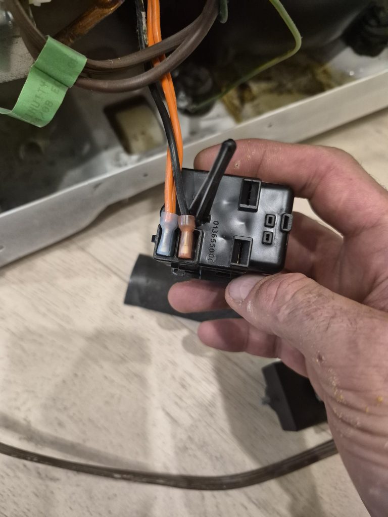 Technician holding a GE fridge compressor start relay during replacement in North York
