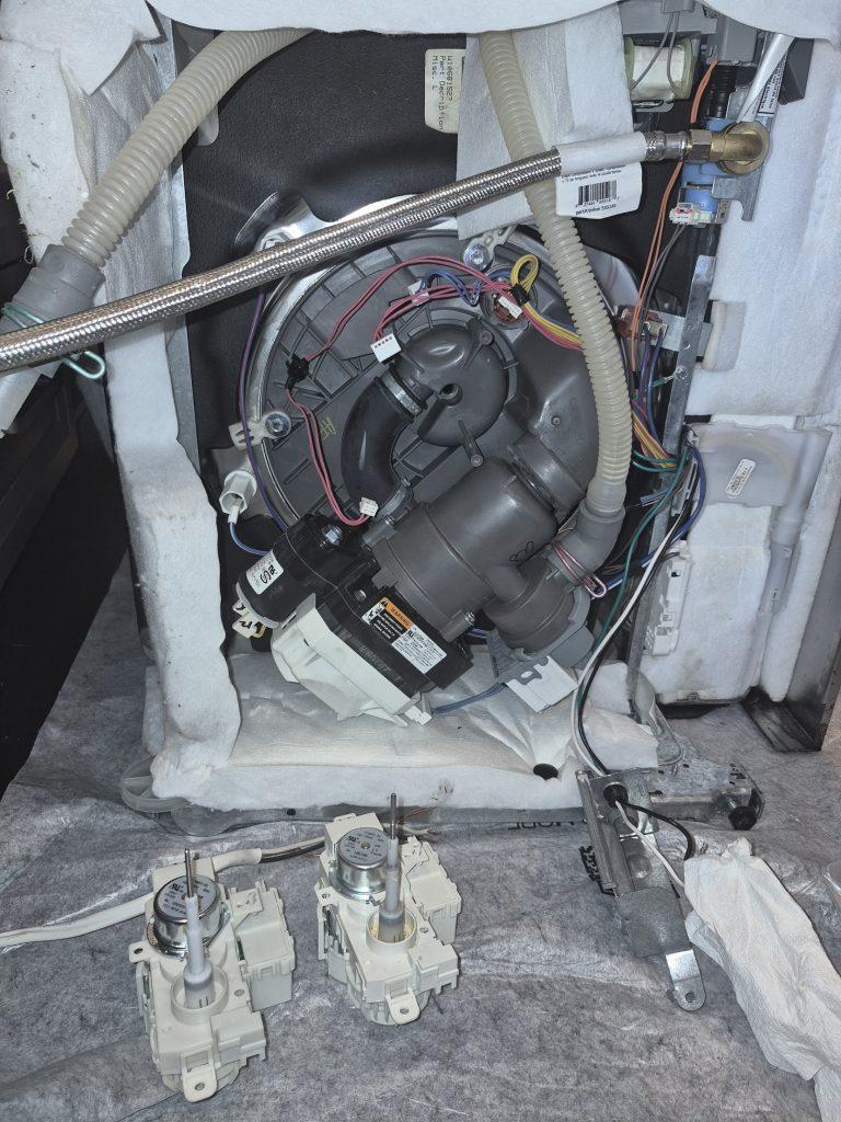 Old and new dishwasher diverter motors next to an opened dishwasher during a leak repair, North York